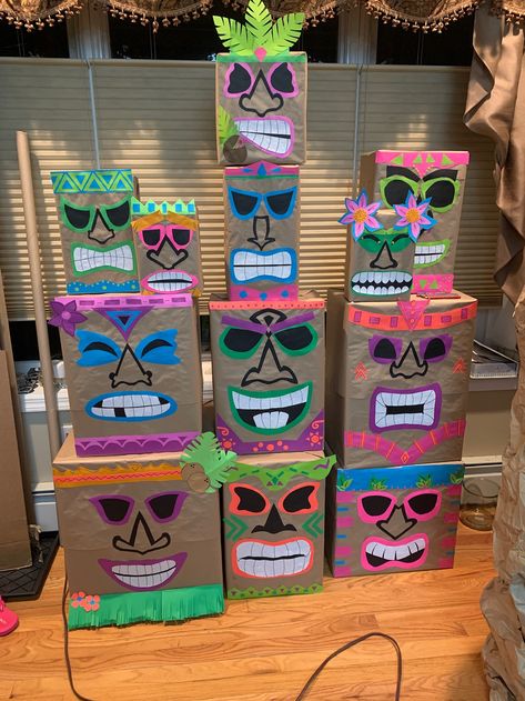 Homemade tiki heads made from assorted cardboard boxes, wrapped in brown craft paper, and decorated with fluorescent card stock paper. Tiki Mask Box, Diy Tiki Mask Cardboard, Tiki Heads Diy Boxes, Cardboard Tiki Totem, Tiki Theme Party Decorations, Diy Cardboard Surfboard, Hawaiian Float Ideas, Tiki Totem Diy, Tiki Boxes Diy