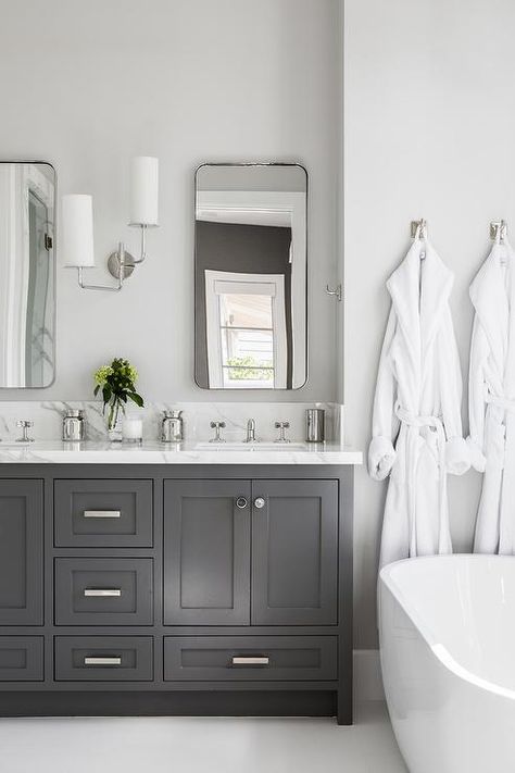 Curved metal vanity mirror flank a polished nickel 2 light sconce mounted to a light gray painted wall over a dark gray dual washstand. Light Grey Painted Walls, Gray Bathroom Walls, Grey Painted Walls, Dark Gray Bathroom, Cabinets Painted, Stand Alone Tub, White Bathroom Cabinets, White Tub, Grey Bathroom Vanity