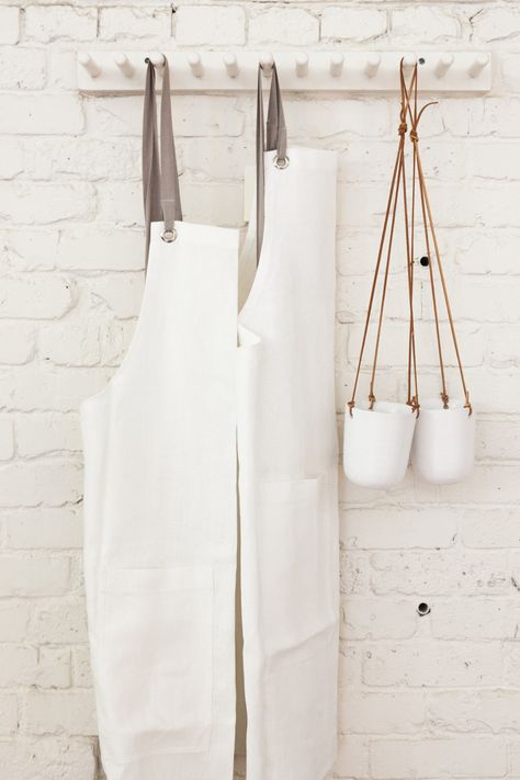 Hanging opposite the retail wall: white linen aprons by Studiopatro and a pair of hanging ceramic planters. Apron Hanging Ideas, Workshop Interior Design, Workshop Interior, Linen Aprons, Diy Wall Hanging Yarn, Kitchen Wall Space, Wall Hanging Ceramic, Peg Rail, Susan Branch