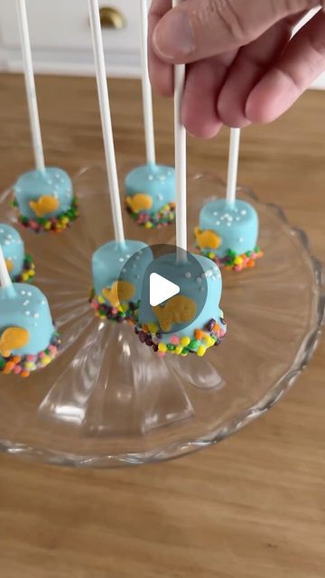 Sheri Wilson on Instagram: "Fish Bowl Marshmallow Pops! 🐠 the perfect treat for a pool party and so easy to make! This is a fun activity the kids can join in with as well! 

Ingredients:
Large marshmallows 
Blue chocolate wafers, melted
Nerds candies
Goldfish crackers
White sprinkles
Lollipop sticks

1. Dip the end of a lollipop stick into the melted chocolate, then press into the marshmallows.
2. Dunk each marshmallow into the melted chocolate and allow the excess chocolate to drip off.
3. Dip the bottom of each marshmallow in Nerds candies for the “pebbles”, then add a goldfish cracker and sprinkles for the bubbles.

#cakepops #marshmallow #easyrecipes #poolparty #summerrecipes #summerfood #summerdessert" Chocolate Dipped Marshmallows On A Stick, Marshmallow Skewers, Sheri Wilson, Large Marshmallows, Dolphin Party, Marshmallow Sticks, Chocolate Dipped Marshmallows, Marshmallow Dip, Nerds Candy