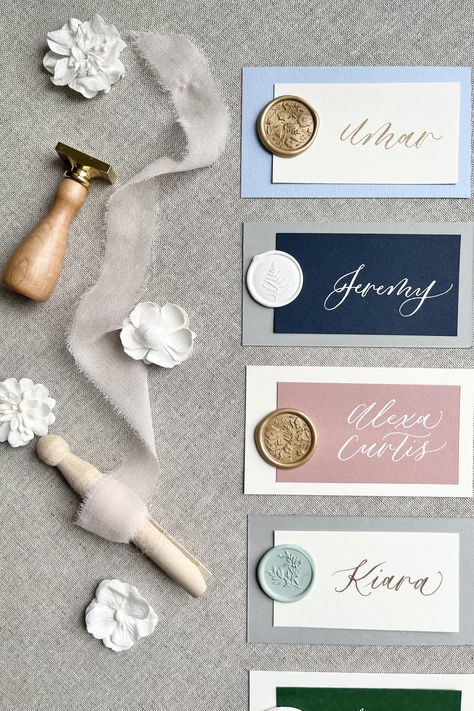 Different colored cardstock with hand-lettered calligraphy on a linen background with ribbon and flower accessories Wedding Name Cards With Wax Seal, Wedding Name Cards Diy, Wedding Guest Place Card Ideas, Wax Seal Place Cards, Creative Place Cards Wedding, Handwritten Place Cards, Calligraphy Place Cards, Place Setting Cards, Table Name Cards