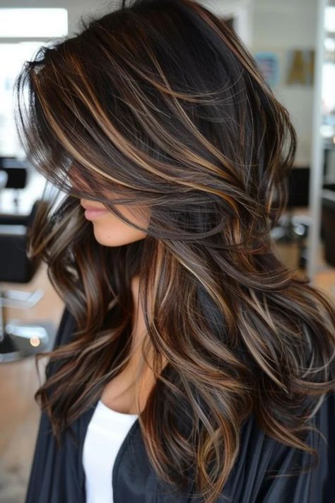 Woman with long, wavy hair featuring brown and blonde highlights in a salon setting. Balayage Hair Blonde To Brown, Black Hair With Golden Brown Highlights, Dark Brown Straight Hair With Caramel Highlights, Rich Dark Brown Hair With Highlights, Dark Hair Balayage Cool Tones, Black With Dark Brown Highlights, Blonde Highlights On Dark Hair Wavy, Black Hair Brown Roots, Dark Brown With Silver Highlights