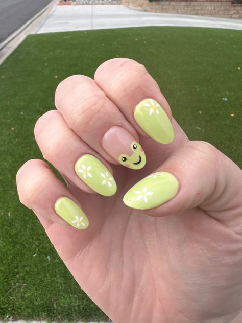 Green grass background. Picture of right hand showing light green nails with white flowers. One fingernail has a drawing of a cartoon frog with blush. Simple Frog Nails, Sage Green Nail Inspo Acrylic, Frog Nail Art Designs, Frog Nail Ideas, Animal Themed Nails, Frog Nails Acrylic, Raccoon Nails, Cute Frog Nails, Frog Nails Designs