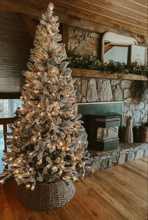 Flocked pre lit Christmas tree with a woven tree collar and a Christmas mantel with a mirror and garland Stone Fireplace Decor, Natural Stone Fireplace, Rustic Christmas Tree Decor, Holiday Mantel Decor, Flocked Tree, Natural Stone Fireplaces, Flocked Christmas Tree, Flocked Trees, Holiday Mantel