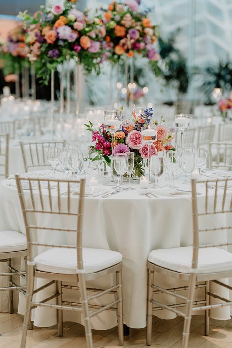 Vivid and bright colors fill the tables with this low style centerpiece on a round table. Round Table Wedding Flower Centerpieces, Colorful Round Table Wedding Decor, Wedding Flower Decorations Round Table, Floral Centrepiece Wedding Round Table, Bright Floral Wedding Centerpieces, Round Table Centerpieces Wedding Summer, Spring Wedding Reception Tables, Low Table Centerpieces Wedding, Wedding Centrepiece Round Table