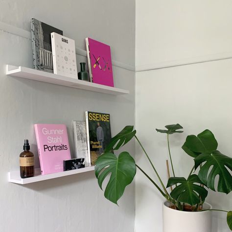 Pictured are 2 shelves on a wall that have colorful books and magazines displayed upright with the covers facing outward. There is also a plant in the corner. How To Fill Empty Wall Space, How To Fill An Empty Wall, Photo Ledge Display, Fill Empty Wall Space, Display Floating Shelves, Picture Ledge Shelves, Floating Shelves White, Picture Ledge Wall, Office Breakout