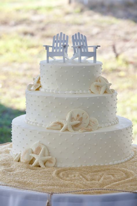 3 tiered wedding cake with swiss dot pattern, small groups of white chocolate sea shells on the tiers, white mini adirondack chairs on top and sugar sand surrounding the wedding cake with initials drawn in the sand Beach Theme Wedding Cakes, Beach Themed Cakes, Beach Wedding Decorations Reception, Nautical Cake, Shells Beach, Beachy Wedding, Beach Cakes, Beach Wedding Cake, Themed Wedding Cakes