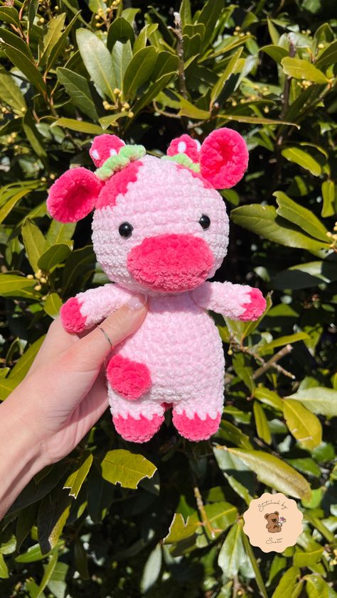 Crochet pink strawberry themed cow made from plush yarn with strawberry horns, light pink body with hot pink patches. Cow is held up in front of a leafy background with natural sunlight. Strawberry Cow Crochet Pattern Free, Strawberry Cow Crochet, Large Amigurumi, Cow Crochet, Crochet Plushies, Strawberry Cow, Amigurumi Plush, Crochet Plushie, Crochet Strawberry