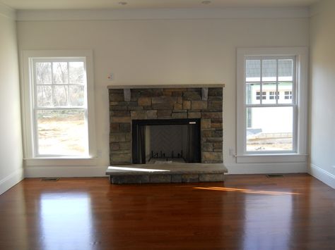 A beautiful stone fireplace is added in the home's living room between two elongated windows letting in extra natural light. Fireplace Between Two Windows, Fireplace Between Windows, Light Flooring Living Room, Apartment Rugs, Yellow Decor Living Room, Interior Window Shutters, Dream House Living Room, Living Room Furniture Tables, Living Room Decor Colors