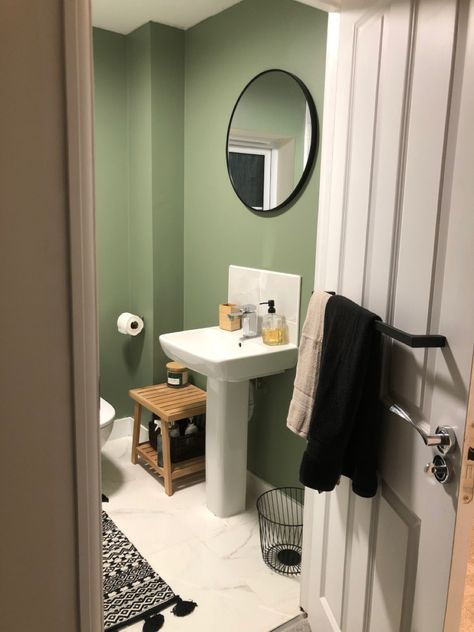 A mid-green coloured bathroom wall, with white ceiling, a large circular mirror with black frame, a scattering of black decor and accessories mixed in with real wood to bring an earthy, natural feeling. Evergreen Bathroom, Rory Bedroom, Flat Painting, Bedroom Ensuite, Bathroom Upgrade, Bathroom Paint, Chinese Evergreen, Flat Ideas, Large Mirror