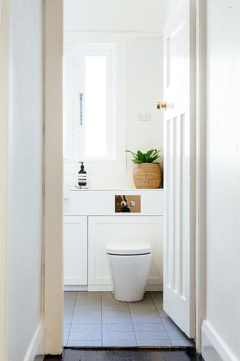 Modern bathroom features a wall-mount toilet atop a gray grid floor placed under windows. Toilet Under Window, Window Above Toilet, Above Toilet, Cheap Patio Furniture, All White Bathroom, Shelves Over Toilet, Bathroom Shelves Over Toilet, Moving Apartment, White Bathroom Designs