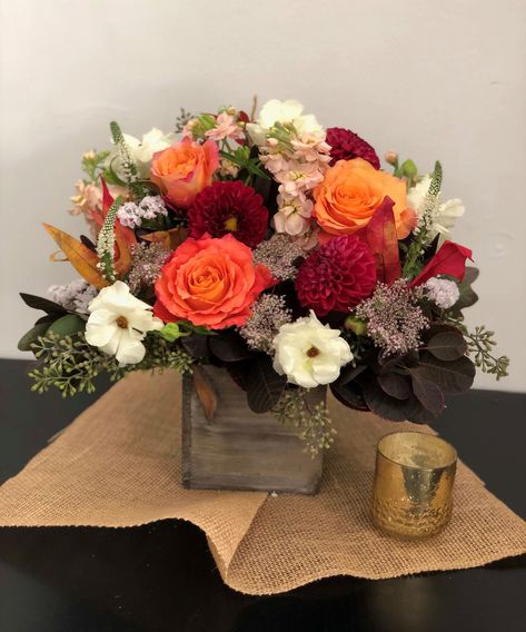 An Assortment of orange roses, burgundy dahlias, peach stock with fillers and fall greens in a wood box. Peach Stock, Poinsettia Care, Burgundy Dahlia, Thanksgiving Flowers, Flowers Centerpieces, Fall Brunch, Florist Logo, Fall Flower Arrangements, Fall Floral Arrangements