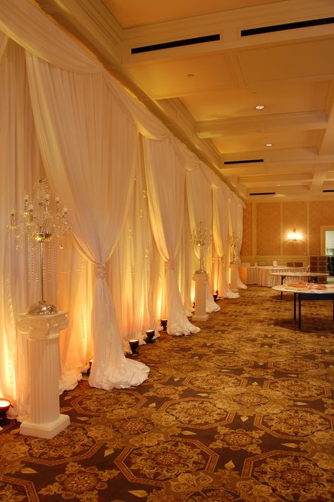 White Backdrop with Amber LED Up Lighting #whitechiffon #fabricbackdrop #amberuplighting #uplighting #AmberLED #weddingbackdrop #weddingdecor #michiganweddings #colonialevents Wedding Wall Drapes, Quince List, Gold Shimmer Background, Yellow Quince, Event Space Decor, Event Draping, Outdoor Christmas Party, Reception Lighting, Uplighting Wedding