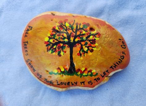 I painted this river rock with an autumn tree. It's a fall color theme, orange, yellow, burgundy, etc. I painted the words, "Fall Trees Show Us How Lovely It Is To Let Things Go."  I have recently decided to clean out and get rid of things that I do not need. It's so hard because so many things hold a memory for me. I really liked the color of the rock so I left the back the natural color. This rock is approximating 4 inches by 3 inches by 0.5 inch It is painted with acrylic paint and sprayed with a clear coat.  I have been a retired bookkeeper for the last five years and enjoy painting and creating. I don't know why rocks speak to me but they do.  I have painted for myself and family for years and I am now enjoying that other people besides family enjoy my artwork.  If you have an idea fo Fall Painted Rocks, Fall Rocks, Let Things Go, Fall Tree Painting, Painted River Rocks, Fall Rock, Inspirational Rocks, Speak To Me, Diy Rock Art