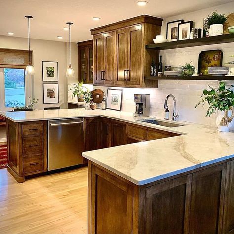 This luscious, wood-toned kitchen is designed with dark-stained cabinetry and a white marble countertop paired with matching floating shelves. The shelves are adorned with rustic accents and mounted on a white subway tile backsplash wall. Potted greenery and rustic, warm wood accents adorn the white marble countertop, contrasting with the light wood flooring that runs throughout. Dark Cabinets With Light Countertops, Kitchen Dark Wood Cabinets, Dark Stained Cabinets, Brown Cupboards, Light Wood Flooring, Dark Wood Kitchen Cabinets, Dark Brown Cabinets, Nice Room, Dark Wood Kitchens