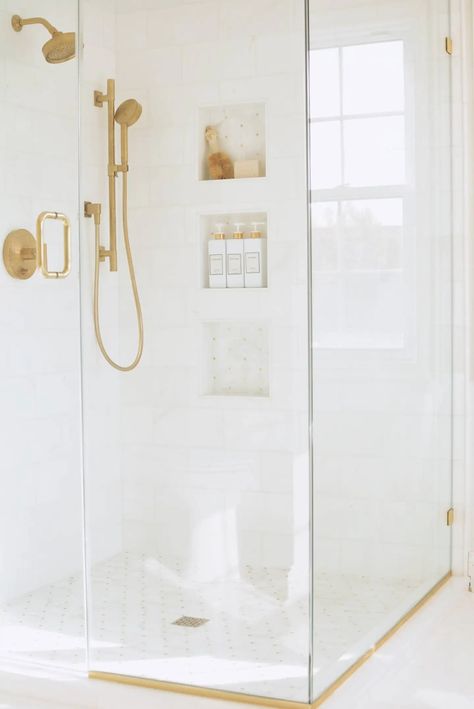 marble shower with glass doors, gold shower fixtures and mosaic shower floor Gold Shower Glass Door, Moen Brushed Gold Shower Fixtures, Gold Shower Fixtures Master Bath, White Shower Gold Fixtures, Moen Shower Fixtures Gold, Gold Shower Niche, White Shower With Gold Fixtures, White And Gold Shower Tile, Shower Fixtures Gold