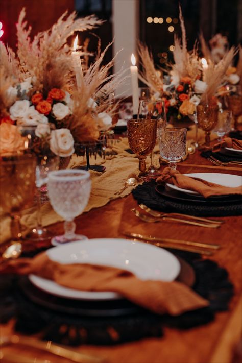 wooden table with black macrame charger, amber and white glass, gold cutlery, terracota napkin and pampas everywhere. Copper And Black Wedding Decor, Burnt Orange And Brown Wedding Decor, Burnt Orange Black And Gold Wedding, Amber And White Wedding, Black White Orange Wedding, Black And Orange Table Setting, Black And Amber Wedding, Rust And Black Wedding Decor, Amber Wedding Decor