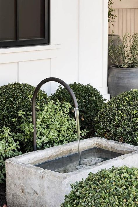 A bronze gooseneck faucet is paired with a concrete water fountain. Concrete Water Feature, Concrete Water Fountain, Backyard Concrete, Hampton Interior, Mindy Gayer Design, Stone Fire Pit, River Rocks, Mediterranean Garden, Garden Studio