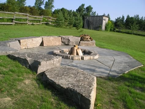 Fire pit built into the slope with armourstone and jumbo limestone flagstone. By Vogel Large Fire Pit Ideas Outdoor Spaces, Fire Pit Built Into Hill, Fire Pit On Sloped Yard, Boulder Fire Pit, Pergola Shade Diy, Outdoor Fire Pit Designs, Fire Pit Landscaping, Stone Fire Pit, Fire Pit Area