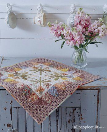 Soft pastel florals and olive green and lavender prints welcome spring in the simple appliqué quilt. Pinwheel Block, Table Topper Patterns, Creeper Minecraft, Mini Quilt Patterns, Hanging Quilts, Spring Quilts, Winter Table, Flower Motifs, Embroidered Quilts