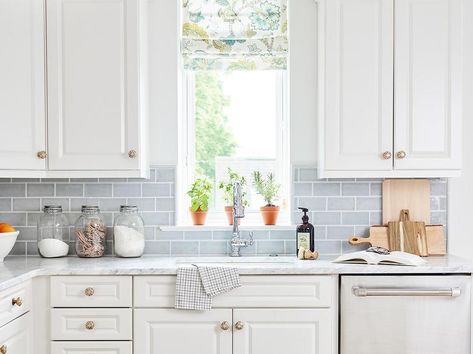 Light blue subway tiled backsplash accents white raised panel cabinets finished with brass knobs and marble countertops. Light Blue Subway Tile, Blue Subway Tile Backsplash, Light Blue Backsplash, Blue Backsplash Kitchen, Blue Subway Tile, Light Blue Kitchens, Marble Counters, Raised Panel Cabinets, Blue Backsplash