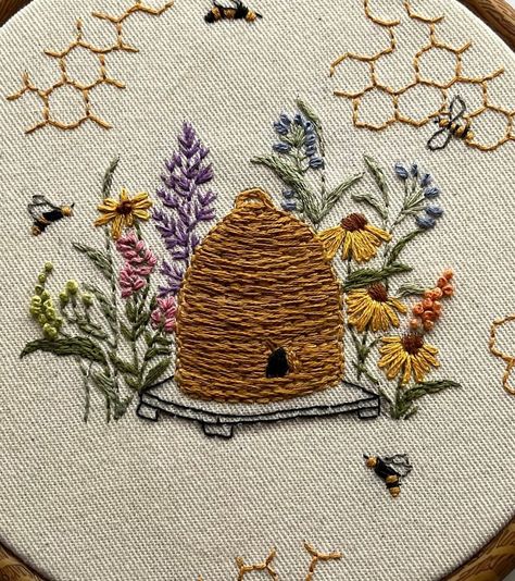 Add a touch of handmade charm to your home with this beautifully embroidered beehive hoop art. This piece features intricate hand-stitched details, including a traditional beehive surrounded by vibrant flowers and busy bees. The honeycomb patterns scattered around the hoop add a whimsical touch. Perfect for nature lovers and embroidery enthusiasts, this art piece is displayed in a wooden embroidery hoop, making it easy to hang on your wall or display on a shelf. The natural, rustic feel of this Honey Bee Wildflowers, Honeycomb Embroidery Pattern, Bee Embroidery Pattern Free, Embroidered Beehive, Beehive Embroidery, Bumble Bee Embroidery Pattern, Bee Hive Art, Bee Hand Embroidery, Honey Bee Embroidery