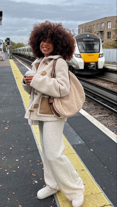 Girl, girl smiling, girl with afro hair smiling, girl with coffee in her hand, girl at the train station, girl in a fall outfit, girl wearing a shearling jacket, girl wearing a knitted jumper, girl wearing knitter trousers, girl wearing clogs, girl clutching a shearling bag, girl in a cozy outfit, girl in a winter outfit, girl in a fall outfit, girl wearing neutral tones, girl in a minimal outfit Shearling Bag Outfit, Cold Lazy Day Outfit, Cozy Winter Outfits Lazy Days, Snow Weather Outfit, Fuzzy Coat Outfit, Outfit Ideas Snow, Outfit Ideas Weekend, Outfit Ideas Lazy, Outfit Inspo Cold Weather