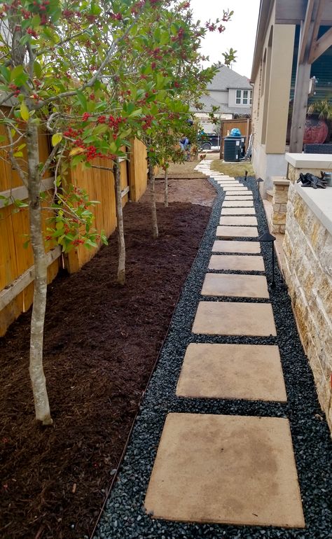 Residential design featuring black stone gravel, leuderstone pavers, mulch beds, Savannah Holly trees Pavers With Rocks In Between Backyard, Black And White Stone Landscaping, Stone And Gravel Patio, Gravel Fence Border, Black Stone Landscaping, Mulch Patio Ideas, Landscaping With Mulch, Black Lava Rocks Landscaping, Savannah Holly