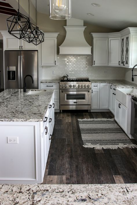 Beautifully elegant white kitchen with gray and black mottled granite and island countertops. The darker wood of the floor really makes the white cabinets, backsplash and countertops stand out. Kitchen Flooring With White Cabinets And Black Countertops, White Kitchen Cabinets With Gray Floors, Black And White Kitchen Makeover, Gray Granite Countertops With Backsplash, White Kitchen Cabinets With Darker Countertops, Gray And Black Granite Countertops, Black And White Kitchen With Granite Countertops, White Granite With White Cabinets, Black Kitchen Cabinets Gray Floor