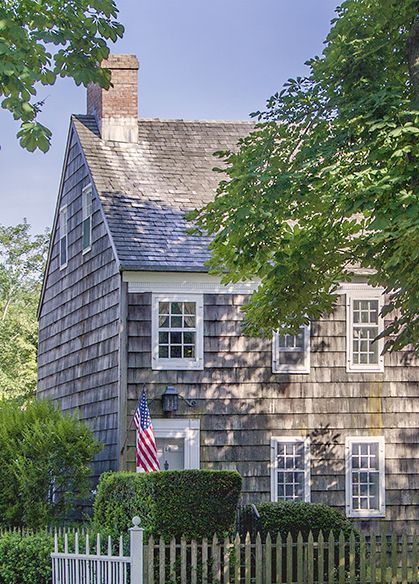 Main Street, East Hampton. A New England house exterior with American flag. COME TOUR MORE Nantucket Style Chic & Summer Vibes! #nantucket #interiordesign #designinspiration #summerliving #coastalstyle New England House Exterior, Nantucket Aesthetic, New England House, New England Cottage, Nantucket Style Homes, England House, Nantucket Cottage, Shingle House, Nantucket Home