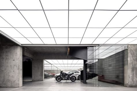 The austere space features exposed concrete beams and a luminous ceiling made of acrylic panels and LEDs. Batman Garage, Concrete Pavilion, Garage Design Interior, Glass Pavilion, Small Spa, Angled Ceilings, Garage Style, Secret Room, Pavilion Design