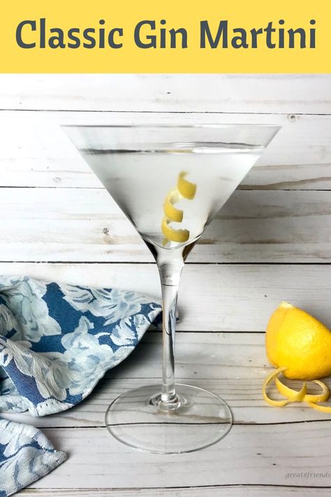 A martini glass with a clear martini in it and a lemon peel and a blue cloth napkin on the side and a half of a lemon on the side.