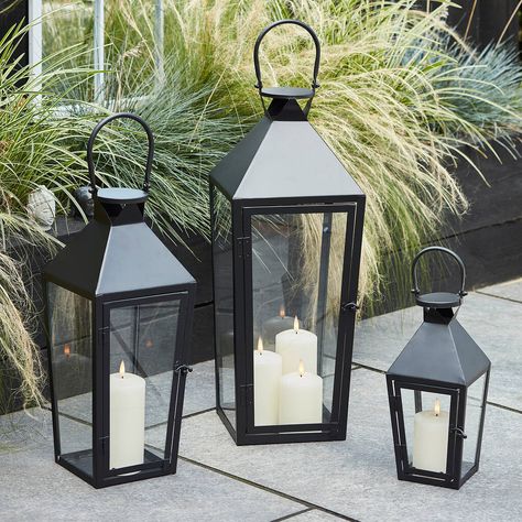 A trio of beautiful black metal garden lanterns, with realistic LED flame candles inside.With a sleek trapeze shape and large handle, style this trio together for a real statement in your garden. Our large lantern features a trio of realistic candles within and the regular and medium sizes feature a single LED candle for a warm ambience each evening. Pop 2 x C batteries (not included) into the base of each candle and opt for the 6 hour timer for automatic illumination each evening.Black metal la Black Lantern Decor, Realistic Candles, Garden Lantern, Lantern Ideas, Large Lanterns, Black Lantern, Candle Base, Garden Lanterns, Outdoor Candles