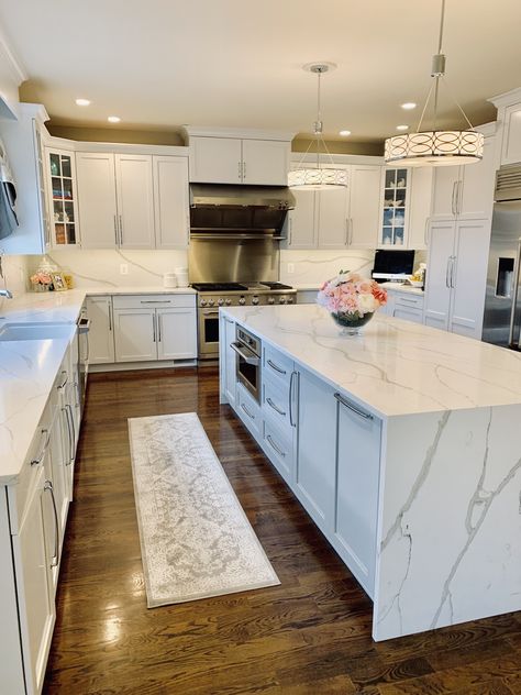 White kitchen done with quartz countertops, backsplash and waterfall island. Stainless appliances and lots of lighting! White Quartz Countertop Waterfall, Modern White Kitchen Design With Island, Waterfall Backsplash Kitchen, White Kitchen Cabinets With Waterfall Island, Kitchen Design Modern White Quartz Countertops, Waterfall Kitchen Counter, White Kitchen With Waterfall Island, Different Countertops In Kitchen Islands, White Quartz Waterfall Island