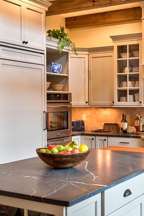 Amazing comfortable kitchen outlined by Green Soapstone countertops and grayish cabinets. The floor is common to look complete hardwood. Also, the backsplash is a tumbled stone tile as well. #greensoapstone #greensoapstonekitchen #greensoapstonekitchencountertop #greensoapstonekitchencounter #offwhitecabinet #creamtumbledtilebacksplash #creambacksplash #darkhardwoodfloor #matefinishgreensoapstone #matefinishgreenkitchentops #mategreencountertops #stonetilebacksplash Soapstone Kitchen Countertops, Kitchen Soapstone, Soapstone Countertops Kitchen, Kitchen Countertops Ideas, Soapstone Kitchen, Stone Countertops Kitchen, Soapstone Counters, Countertops Ideas, Soapstone Countertops