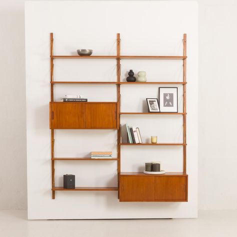 Visually appealing and extremely functional, this shelving system in teak was designed in the style of 1970s projects by Poul Cadovius for Cado. The wall unit is crafted from warm-hued teak wood, showcasing beautiful grain patterns. Use of teak veneer ensures sturdiness and longevity. The combination of shelves and cabinets with sliding doors makes this wall unit an excellent storage option for your studio, living room, or bedroom, offering functionality without compromising on style or space. T Wall Shelving Unit Living Room, Cabinets With Sliding Doors, Shelving Units Living Room, Mid Century Wall Unit, Studio Living Room, Teak Wall Unit, Modular Cabinets, Wall Shelving Units, Teak Wall