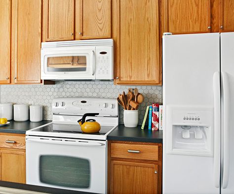 Working It Updating surfaces and bringing in subtle color gave this small kitchen big style without breaking the bank. The appliances, cabinets, floors, and lights were in good working condition, so they stayed. A fresh coat of gray paint on the walls in the same hue as the tile, but lighter, makes the room feel spacious. Paint Honey Oak Cabinets, Wall Colors With Oak Cabinets, Kitchen Updates On A Budget, Colors With Oak Cabinets, White Kitchen Appliances, Honey Oak Cabinets, Paint Walls, Painting Oak Cabinets, Kitchen Updates