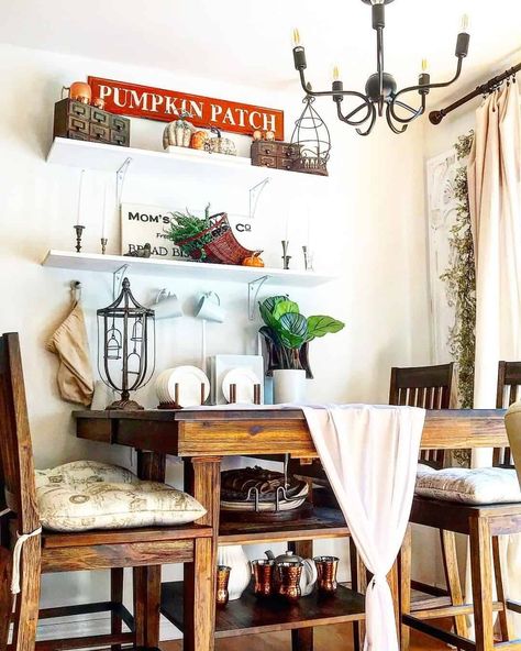 A warm amber-stained wood dining table set is decorated with a white cotton table runner and tie-on cushions. A set of white open-faced shelves are installed along the wall behind the table. Decorate shelves like these with warm fall decor, indoor plants, dinnerware displays, and candles...   Image: thyme_and_tinsel Minimalist Dining Room Decor, Fall Decor Indoor, Warm Fall Decor, Dinnerware Display, Creative Dining Room, Decorate Shelves, Wood Dining Table Set, Dining Hutch, Small Dining Room