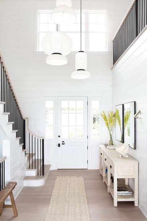 A white front door accented with 9 glass panels is flanked by sidelights and opens to a foyer boasting white shiplap walls and staggered white lights hug over a fringe jute runner. Pretty Beach House, Style Me Pretty Living, Timeless Interiors, Custom Furniture Design, Foyer Decorating, Entry Way Design, Ship Lap Walls, Beach House Decor, Long Island