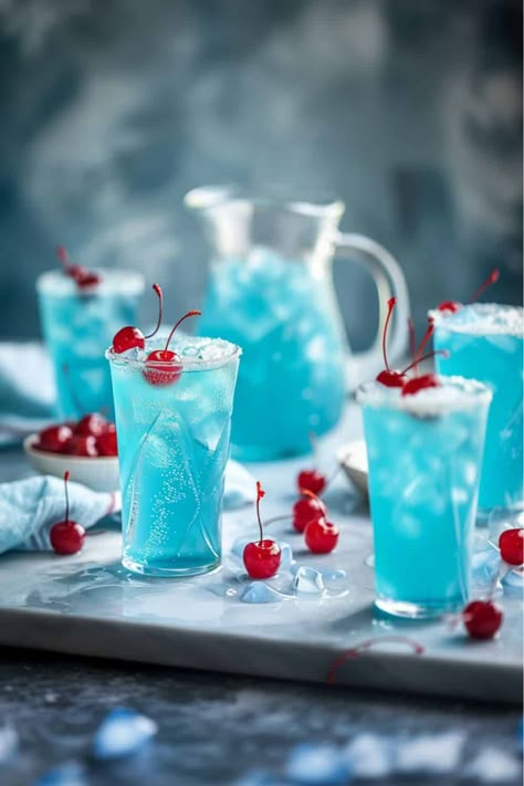 Blue Hawaiian Rum Punch, This image features a clear pitcher filled with a vibrant blue punch, surrounded by four glasses each brimming with the chilled beverage and ice. A Maraschino cherry adorns the top of the ice in each glass, adding a splash of red to the cool blue, creating a festive and inviting display. Tropical Punch Recipe, Pineapple Lemonade Punch, Blue Hawaiian Punch, Vodka Cocktails Easy, Blue Punch, Rum Punch Recipes, Lemonade Punch, Ginger Lemonade, Pineapple Lemonade