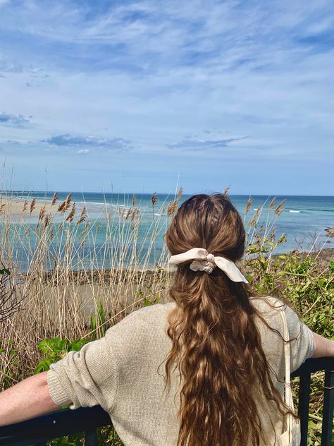 girl staring out over the water, long brown hair with ribbon facing the camera Seaside Grandma Aesthetic, New England Girl Aesthetic, Coastal Preppy Aesthetic, Coastal Granddaughter Hair, Coastal Town Outfit, Cottagecore Beach Aesthetic, Coastal Academia Aesthetic, Small Coastal Town Aesthetic, Old Summer Aesthetic