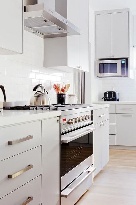 Light gray flat panel drawers painted in Farrow & Ball Pavilion Gray are fitted with satin nickel pulls and a white quartz countertop and flank a stainless steel oven rage fixed against an all white subway tile backsplash beneath a stainless steel hood. Flat Front Kitchen Cabinets, Flat Panel Kitchen Cabinets, Flat Front Cabinets, Flat Cabinets, Pavilion Grey, Espresso Kitchen Cabinets, Rustic Backsplash, Farmhouse Backsplash, Beadboard Backsplash