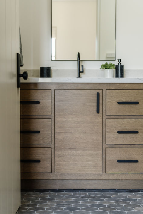 Custom oak vanity with inset cabinets, black hardware and fixtures, and honeycomb grey tile bathroom floor. #thedendesigngroup #bathroomvanity #vanity #blackhardware #cabinethardware #bathroomfloor #honeycombtile #bayareainteriordesign Wood Vanity Black Hardware, Brown Vanity Black Hardware, Wood Vanity Gray Floor, Bathroom Grey Tiles Wood Vanity, Grey Tile Bathroom Floor Wood Vanity, Hex Tiles Bathroom, Vanity In Bathroom, Honeycomb Tile, Grey Bathroom Tiles