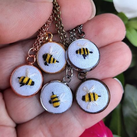 Hand holding 5 small round pendants attached to necklace chain.  The pendants feature tiny hand embroidered yellow and black bees with white wings. Bee Necklaces, Bees Embroidery, Trinket Ideas, Hand Embroidered Necklace, Embroidered Bee, Embroidered Jewelry, Embroidered Necklace, Bee Necklace, Slow Stitching