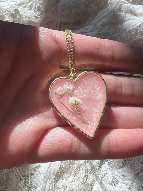 "Preserved baby's breath flowers over a pool of shimmering light-pink. All in a gold heart pendant with gold chain.  Baby's breath flowers are a symbol of everlasting love. 💗  Heart pendant is 1.25 inches wide. Gold chain is 16\" plus 2\" extender.  Chain is nickel free, hypoallergenic, and rust free.  Small jewelry box included.  Hand made with love :)" Resin Pendant Ideas, Cute Pink Resin Necklace, Resin Art Pendant, Resin Heart Charm Pendant Jewelry, Diy Crystal Crafts, Resin Jewelry Pendants, Handmade Heart-shaped Resin Jewelry, Heart-shaped Resin Necklace For Valentine's Day, Resin Necklaces