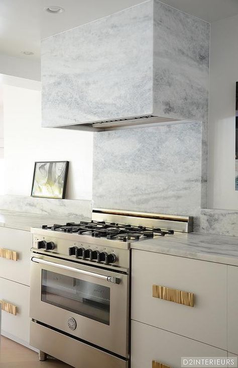 Contemporary kitchen features a white cabinets adorned with gold hardware topped with gray marble flanking stainless steel stove under a grey marble backsplash and a gray marble vent hood. Grey Marble Kitchen, Replacing Kitchen Countertops, Quartz Backsplash, White Marble Kitchen, Stove Backsplash, Small Kitchen Layouts, Marble Kitchen, Marble Backsplash, Kitchen Images