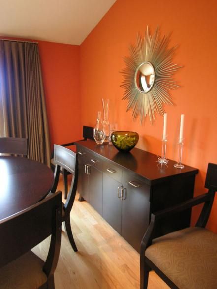 The dark wood dining set and buffet are a sweet complement to pumpkin orange walls in this chic dining room. A gold sunburst mirror echoes the natural tones of the orange walls, while enhancing the overall color scheme. Clear, glass accessories are a neutral accompaniment to the room and avoid interrupting the vibrant wall color. Design by Velvet Hammerschmidt Orange Dining Room, Orange Rooms, Living Room Decor On A Budget, Chic Dining Room, Living Room Orange, Room Blue, Orange Decor, Mirror On The Wall, Orange Walls