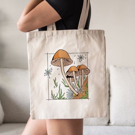 This Mushrooms Tote Bag is a stylish upgrade to reusable tote bags.  This Cottagecore Inspired mushroom canvas tote bag make a great reusable tote for yourself or as a gift tote.  ⚡ USA fast delivery. We deliver within a week. ⚡ Our Tote Bags are made with 100% cotton sheeting. Add their reinforced handle stitching to the mix, and you got a reliable bag rich in both practicality and durability. These durable totes are crafted with a last technological DTG printer for a vibrant flawless finish. T Tote Bag Ideas Design, Beach Tote Bags Diy, Tote Bag Design Ideas, Autumn Tote Bag, Mushroom Canvas, Diy Tote Bag Design, Handpainted Tote, Mushroom Tote Bag, Bachelorette Tote Bags