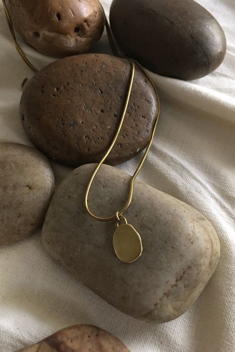 This classic brass necklace features an organic shaped pendant suspended on a snake chain. Named after 'pebble' in Arabic, it is an ode to both the structured and natural world. The more delicate sister style to the Hasaa Major Necklace. Details: 18” chain Solid brass Handcrafted artisan quality Lightweight, comfortable Learn about brass jewelry care tips here. Process: This piece is fabricated by hand in St. Louis, MO using domestically-sourced, durable solid brass. Because this piece is made t Artistic Jewelry Photography, Jewelry Pictures Photography, Pendant Photography Ideas, Jewelry Props Photography, Jewelry Still Life Photography, Jewelry Photography Styling Instagram, Jewellery Product Shoot, Necklace Shoot, Jewelery Shoot