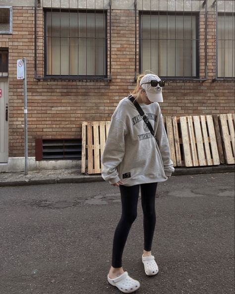 slouchy oversized college jumper, white crocs and black leggings. Accessories are black sunglasses cream hat and hair is pulled back into a ponytail Crocs For Women Outfit, Legging Crocs Outfit, Black Leggings And Crocs Outfit, Croc Airport Outfit, Leggings Crocs Outfit, Crocs Ootd Women, Crocs Outfit Leggings, Styling White Crocs, Classic Crocs Outfit